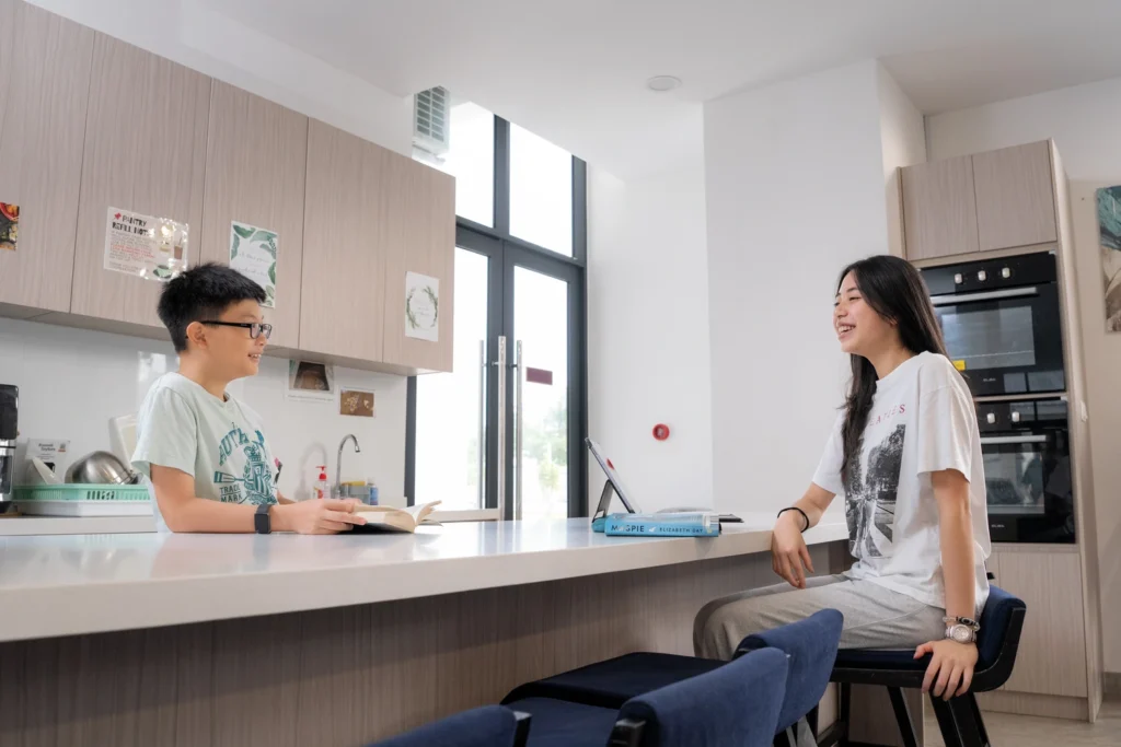 Two boarders chat while studying at the kitchenette counter.