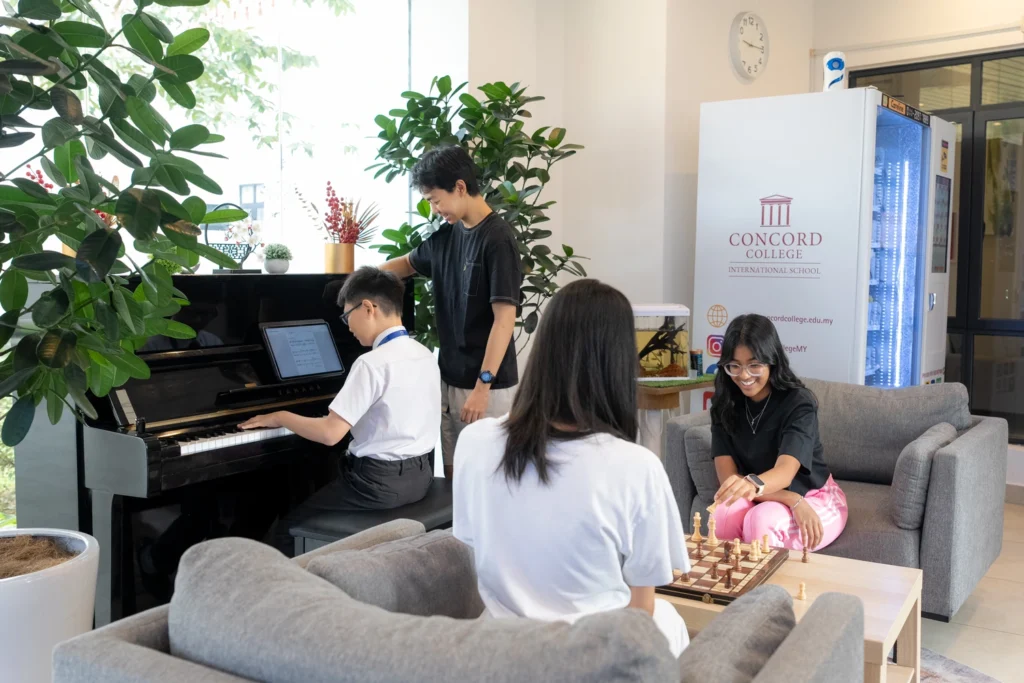 Boarders in the common room, one at the piano while others gather over a game of chess.