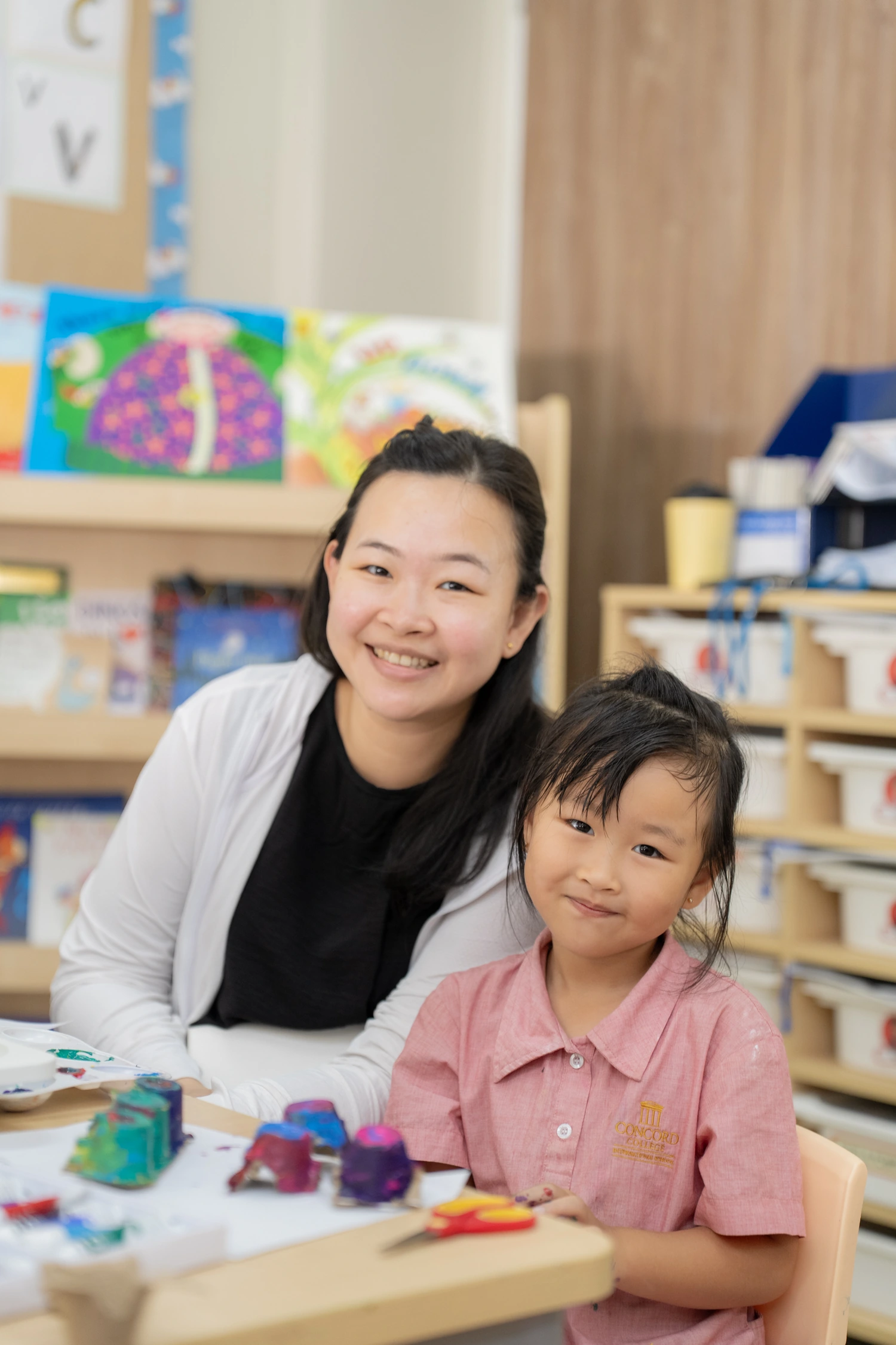 A parent smiles with her daughter during a school craft session.