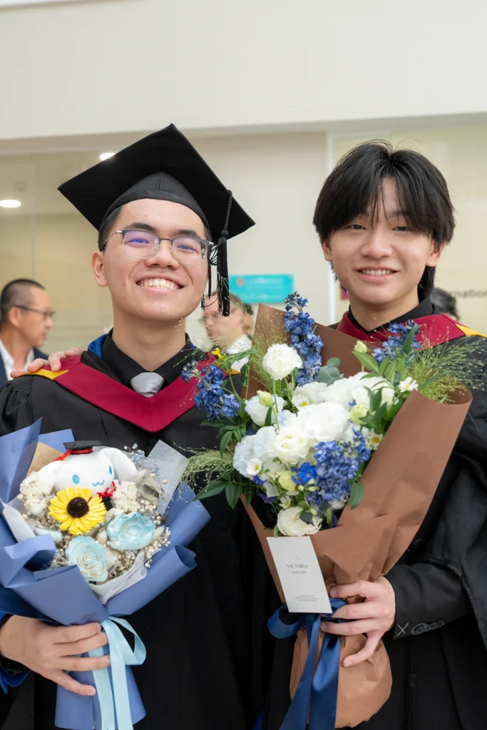 Two graduates smile with their bouquets at the graduation ceremony.