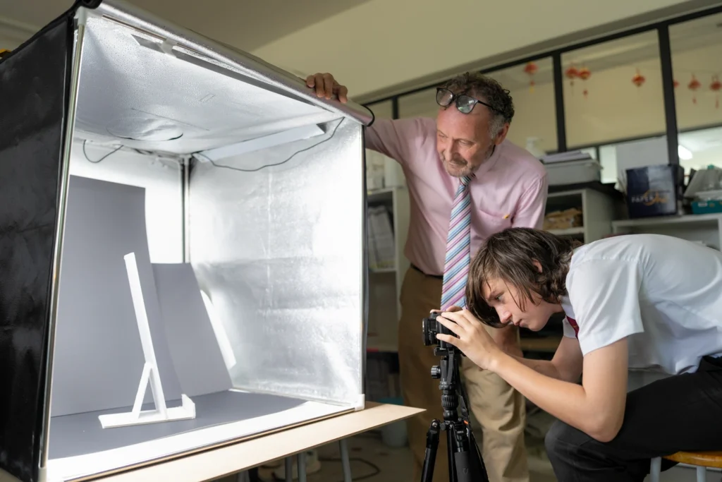 Design and technology students photographing their models in a studio light tent with their teacher.