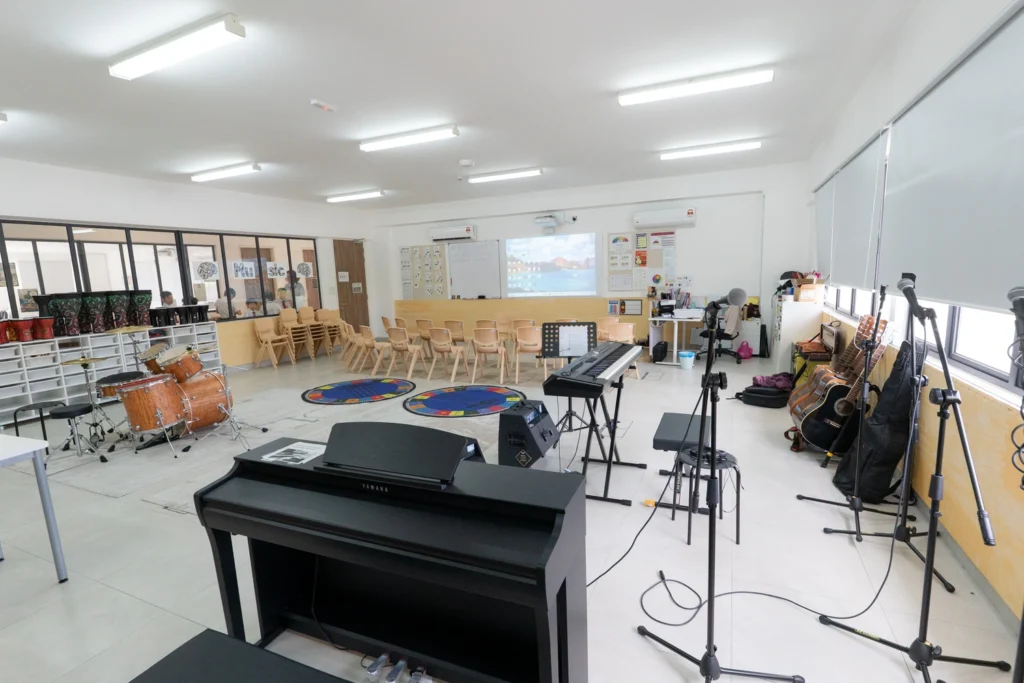 The music classroom with a piano, drum kit, keyboards, guitars and microphone stands.
