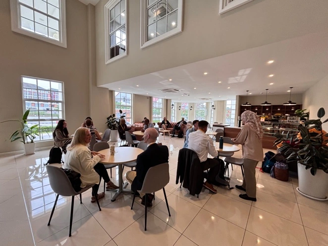 Staff and visitors seated at tables in the atrium cafe beneath the tall arched windows.