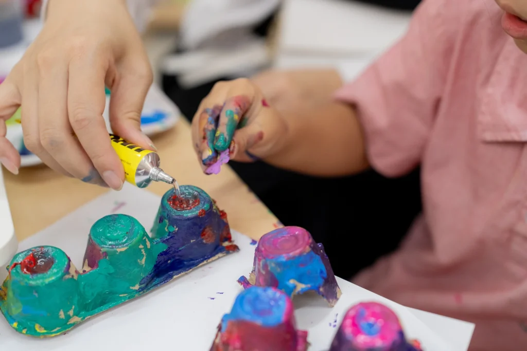 A child paints an egg-carton caterpillar during a hands-on classroom activity.