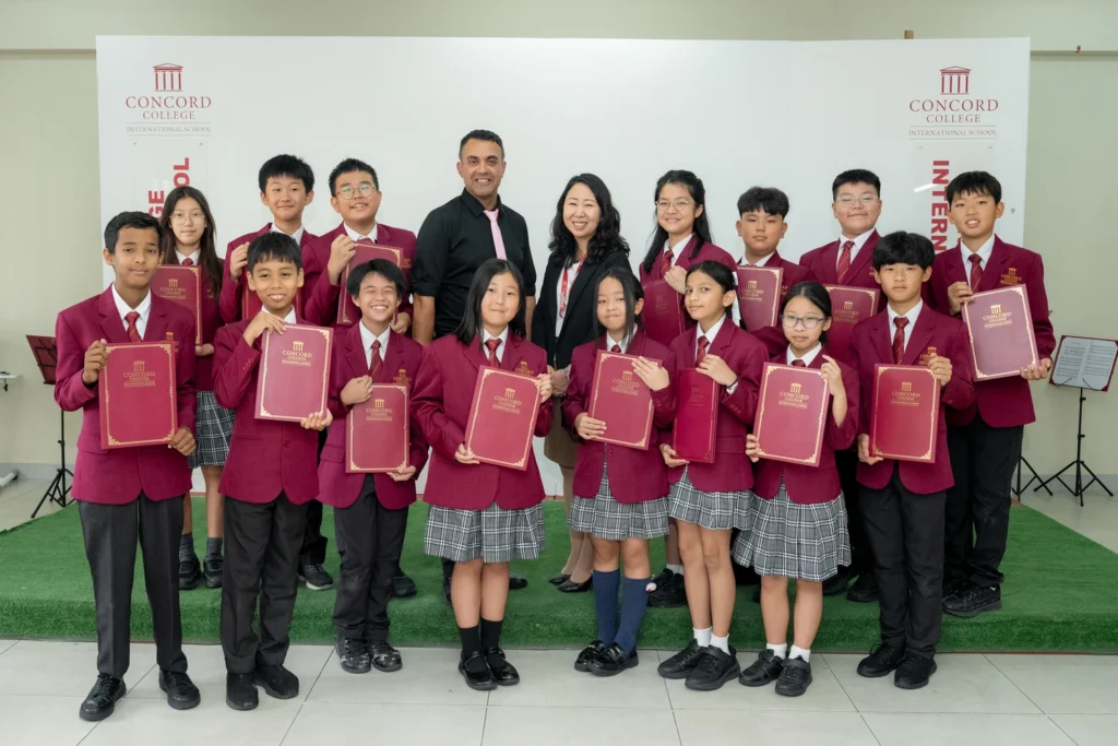 A group of students in maroon blazers holding certificates at an event.