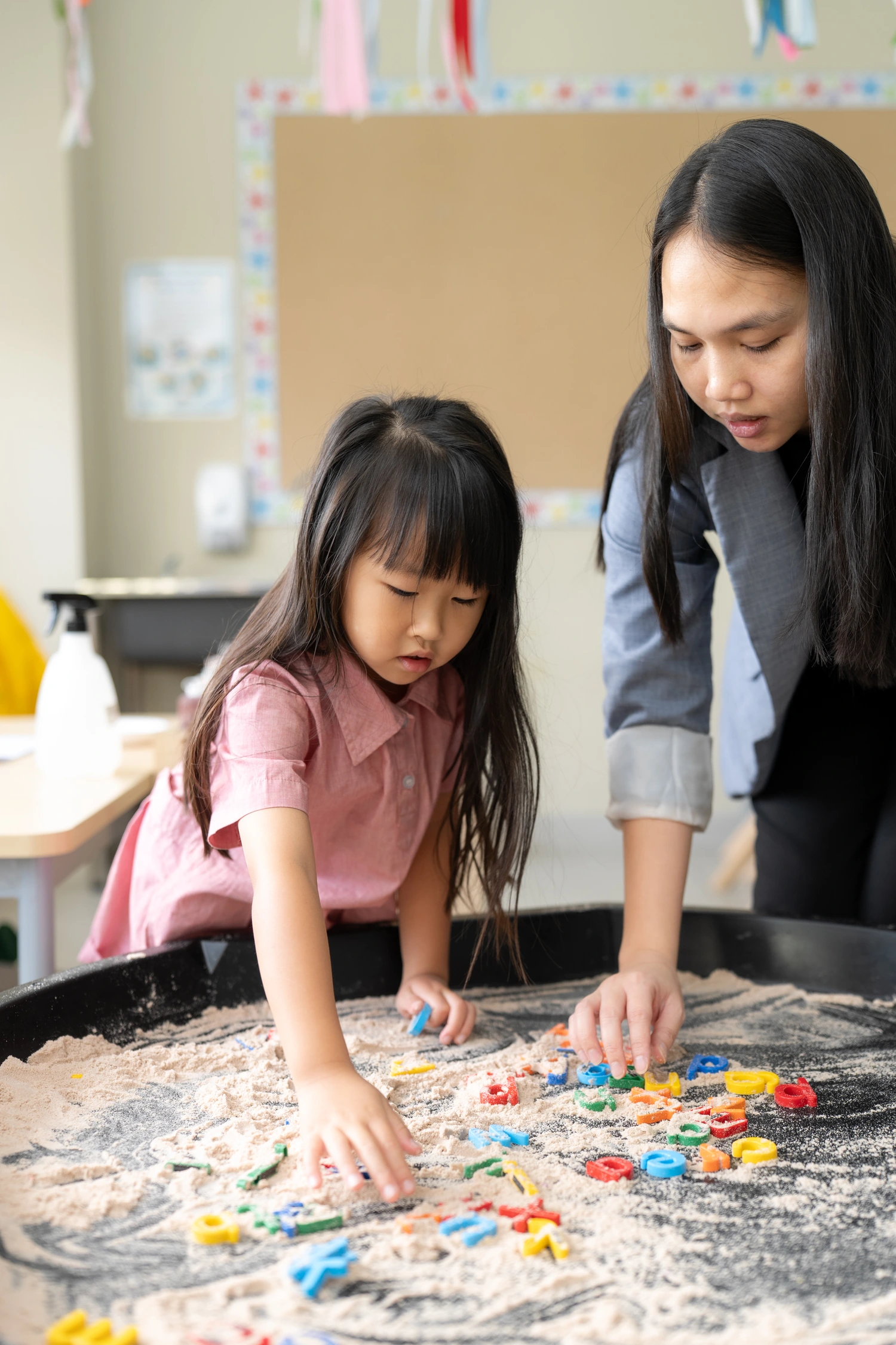 A teacher and a Reception pupil find letters in the sand tray.